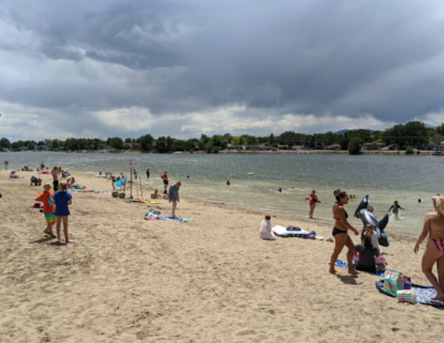 A sandy beach scene with people sunbathing, swimming, and playing in the water under a cloudy sky.