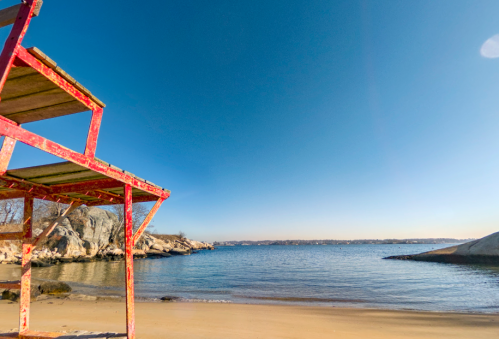 A vibrant red structure on a sandy beach with calm blue water and a clear sky in the background.