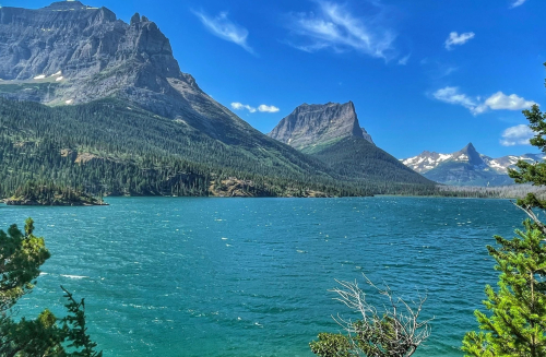 A serene lake surrounded by lush green mountains under a bright blue sky with scattered clouds.