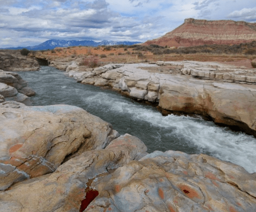 A winding river flows through rocky terrain, with layered cliffs and a cloudy sky in the background.