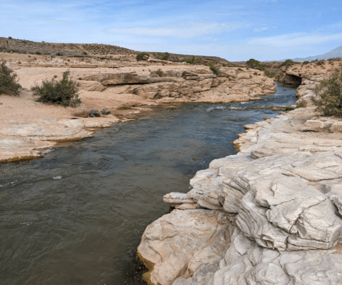 A winding river flows through rocky terrain under a clear blue sky, surrounded by sparse vegetation.