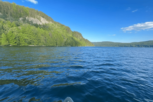 A serene lake surrounded by lush green hills under a clear blue sky. Gentle waves ripple across the water's surface.