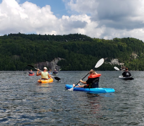A group of people kayaking on a calm lake surrounded by green hills and a partly cloudy sky.