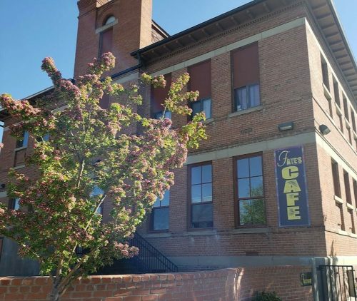 A brick building with a sign reading "Faye's Cafe" and a flowering tree in front.