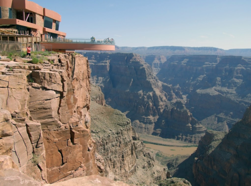 A view of a canyon from a cliffside observation deck, showcasing steep rock formations and a river below.