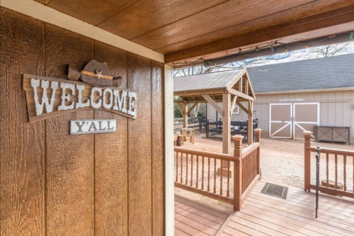 A wooden sign reading "Welcome Y'all" hangs on a rustic wall, leading to a barn and outdoor area.
