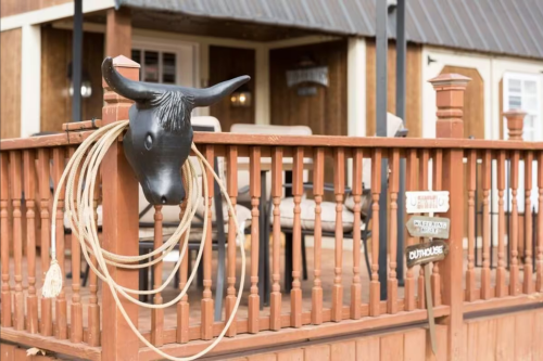 A rustic wooden porch with a bull's head decoration and ropes, featuring seating and a sign.