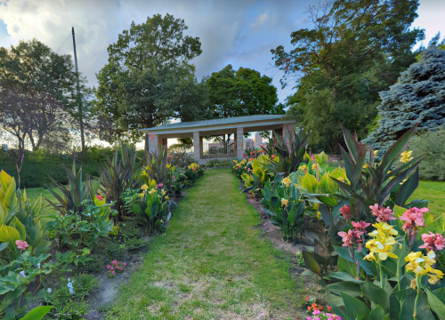 A lush garden path lined with colorful flowers leads to a gazebo surrounded by trees and greenery.