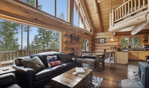 Cozy log cabin interior with large windows, wooden furniture, and a warm, inviting atmosphere.