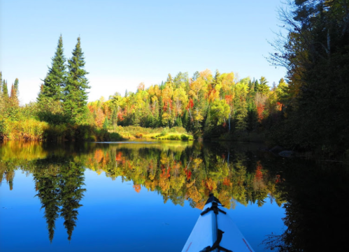 A serene lake reflects colorful autumn trees under a clear blue sky, with a kayak in the foreground.