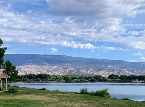 Scenic view of a calm lake surrounded by green trees and mountains under a partly cloudy sky.