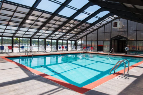 Indoor swimming pool with clear walls and ceiling, surrounded by lounge chairs and a view of the outdoors.