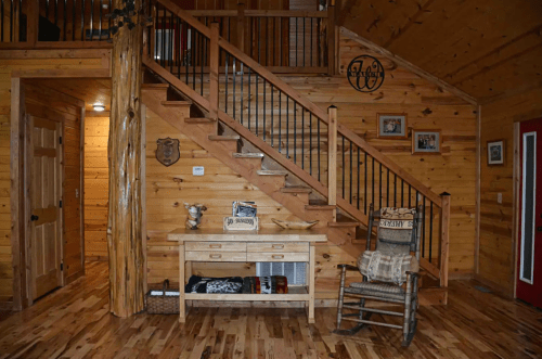 Cozy wooden interior featuring a staircase, a rustic table, and a rocking chair against a warm, natural wood backdrop.