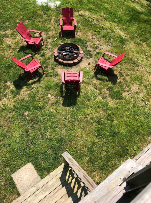 Aerial view of a grassy area with a circular fire pit surrounded by red Adirondack chairs.