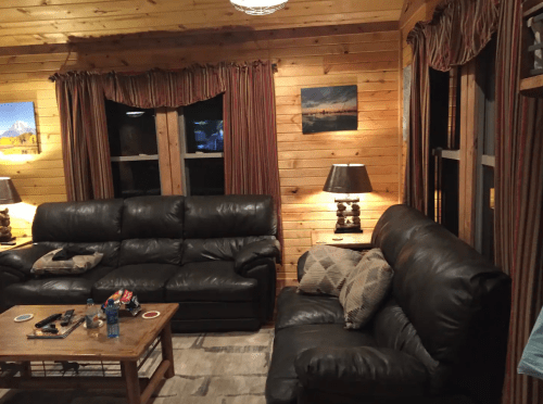 Cozy wooden living room with leather sofas, lamps, and framed artwork on the walls. Warm, inviting atmosphere.