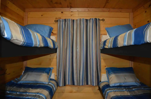 A cozy cabin interior with two sets of bunk beds and striped curtains, featuring blue and beige bedding.