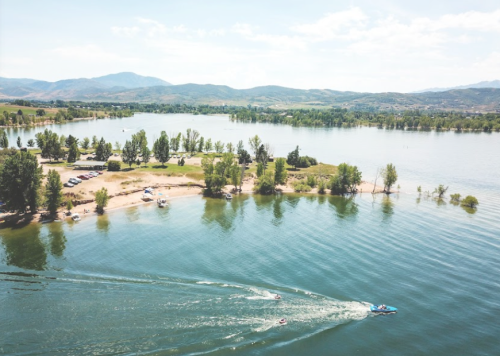 A scenic view of a lake with a boat, surrounded by trees and mountains under a clear blue sky.
