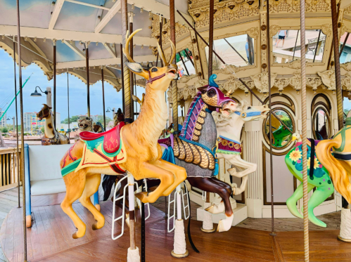 Colorful carousel animals, including a deer and a horse, inside a vintage carousel structure. Bright sky in the background.