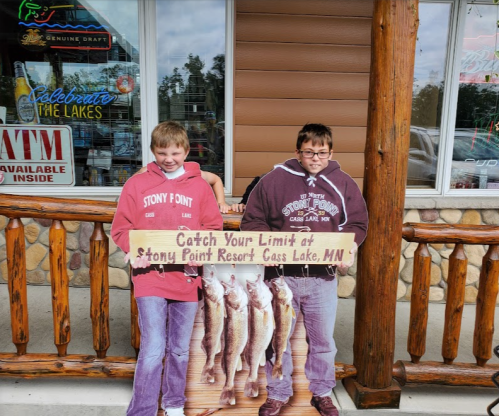 Two boys stand outside a lodge holding a sign that reads "Catch Your Limit at Stony Point Resort, Cass Lake, MN."