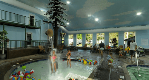 Indoor pool area with children playing, colorful balls, and a waterfall feature under a painted sky ceiling.