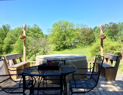 A sunny outdoor deck with a hot tub, surrounded by green trees and a clear blue sky.