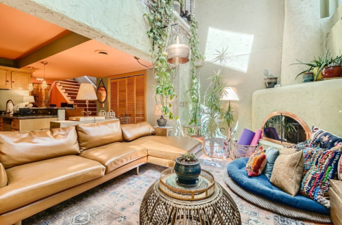 Cozy living room with a large brown sofa, plants, and colorful cushions, featuring a warm, inviting atmosphere.