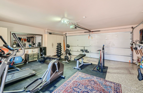 A spacious garage gym with exercise equipment, including weights, a treadmill, and a rowing machine, on a patterned rug.