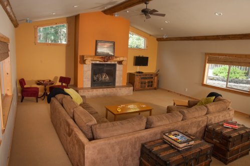 Cozy living room with a large sectional sofa, fireplace, and windows, featuring warm colors and rustic decor.