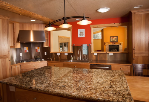 Modern kitchen with wooden cabinets, granite island, stainless steel appliances, and warm orange accents.