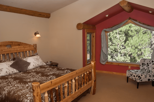Cozy bedroom with a wooden bed, patterned bedding, and a large window overlooking greenery.