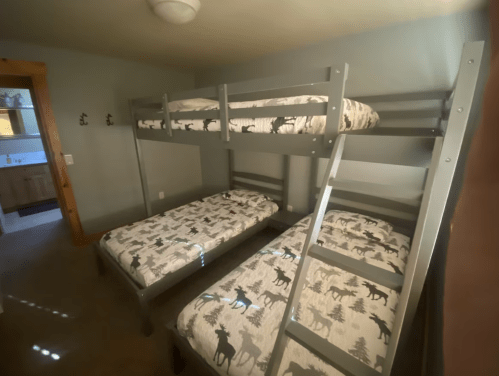 A cozy bedroom featuring a gray bunk bed and two twin beds with patterned bedding, set in a softly lit space.