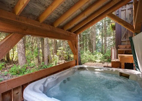 A cozy hot tub under a wooden shelter, surrounded by lush trees and nature.