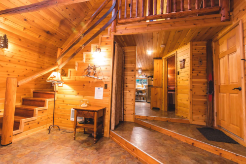 Cozy wooden interior of a cabin with stairs, warm lighting, and a welcoming entrance.