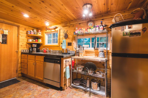 Cozy wooden kitchen with stainless steel appliances, shelves of bottles, and pots, illuminated by warm lighting.