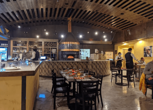 Interior of a cozy restaurant featuring a wood-fired oven, wooden beams, and tables set for dining.
