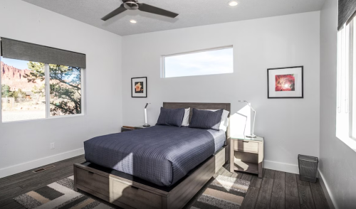 A modern bedroom with a queen bed, two lamps, and large windows showcasing a scenic view outside.