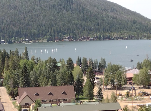 A scenic view of a lake surrounded by trees and mountains, with sailboats on the water and buildings in the foreground.