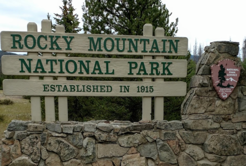 Sign for Rocky Mountain National Park, established in 1915, with a stone base and a National Park Service emblem.