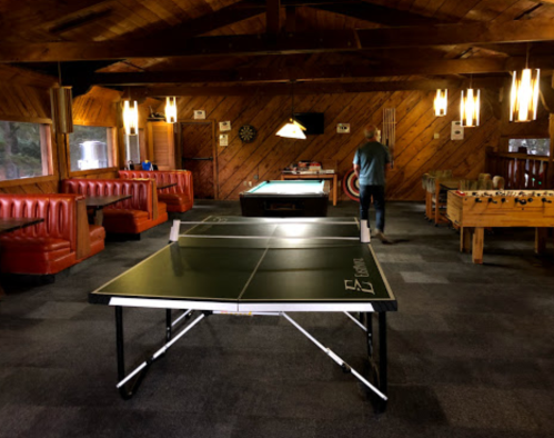A cozy game room featuring a ping pong table, pool table, foosball table, and wooden decor.
