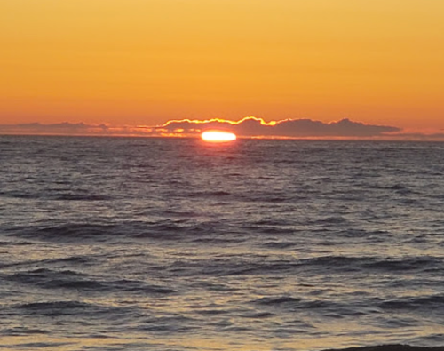 A serene sunset over the ocean, with the sun partially hidden behind clouds, casting warm colors across the sky.