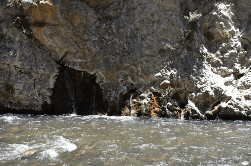 A rocky riverbank with flowing water and a small waterfall cascading from the cliffside.