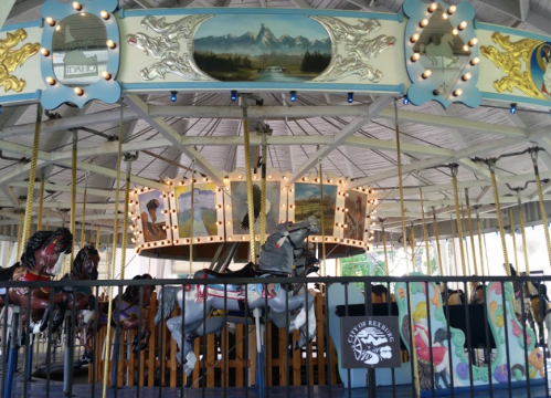 A vintage carousel with painted horses and scenic artwork, set under a wooden pavilion.