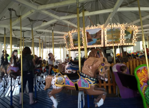 A carousel with colorful horses, surrounded by people enjoying the ride in a lively amusement park setting.