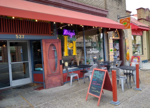 A cozy café with outdoor seating, colorful signage, and a chalkboard menu, located on a charming street.