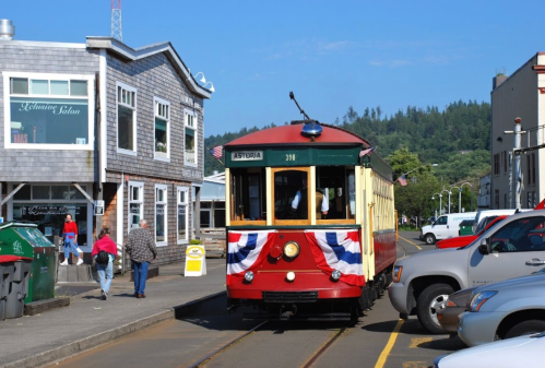 A vintage tram decorated with bunting, parked near shops and people on a sunny day in Astoria.