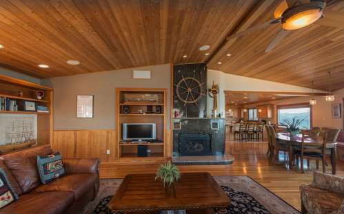 Cozy living room with wooden ceiling, leather sofa, fireplace, and open layout to dining area with nautical decor.