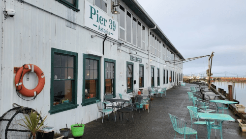Exterior view of Pier 39 in Astoria, featuring a waterfront walkway with green chairs and a lifebuoy.
