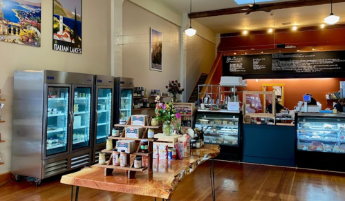 A cozy café interior featuring display cases, a wooden table with products, and colorful wall art.