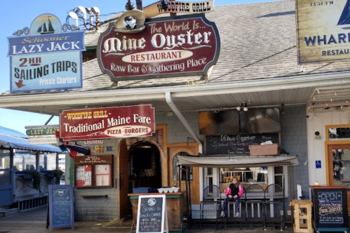 A restaurant facade with various signs, featuring outdoor seating and a person sitting at a table.