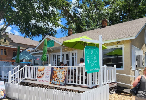 A cozy restaurant with outdoor seating, green umbrellas, and a sign reading "Mr. Gene's Beans" on a sunny day.